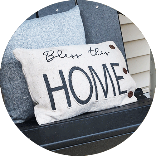 A pillow that says Bless This Home, with three buttons on one side.